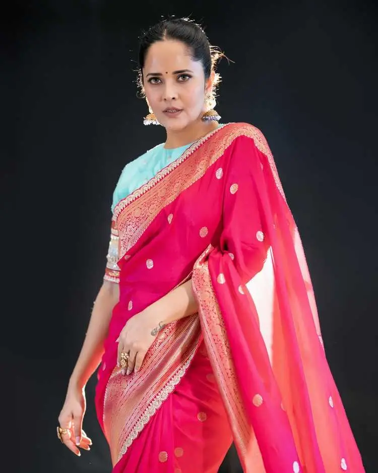 Anasuya Bharadwaj striking a confident pose, highlighting the rich fabric and golden details of her ethnic attire.